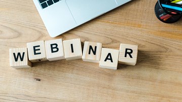 Träklossar på skrivbord bredvid laptop som bildar ordet webinar.