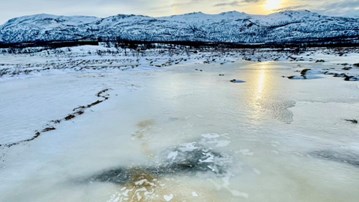 Ett fruset vattendrag med fjäll i bakgrunden.