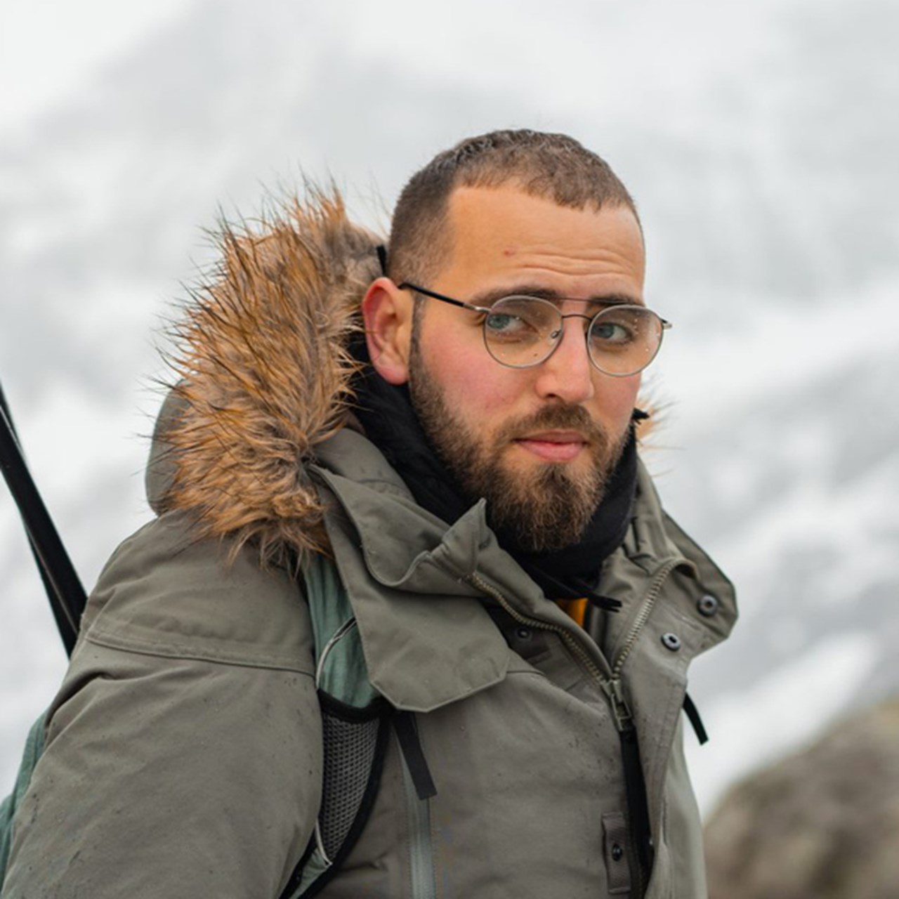 En man med skägg, iklädd jacka och med ett par skidstavar i handen.