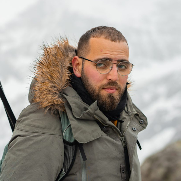 En man med skägg, iklädd jacka och med ett par skidstavar i handen.