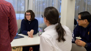Sophia Harlid sits at a white table and smiles while talking to three researcher who have their backs to the camera.