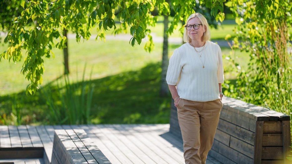 Kvinna går utomhus med grönska runt sig och tittar åt sidan.
