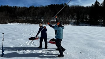 Tre människor för en lång borr ned i ett hål i isen på en sjö.