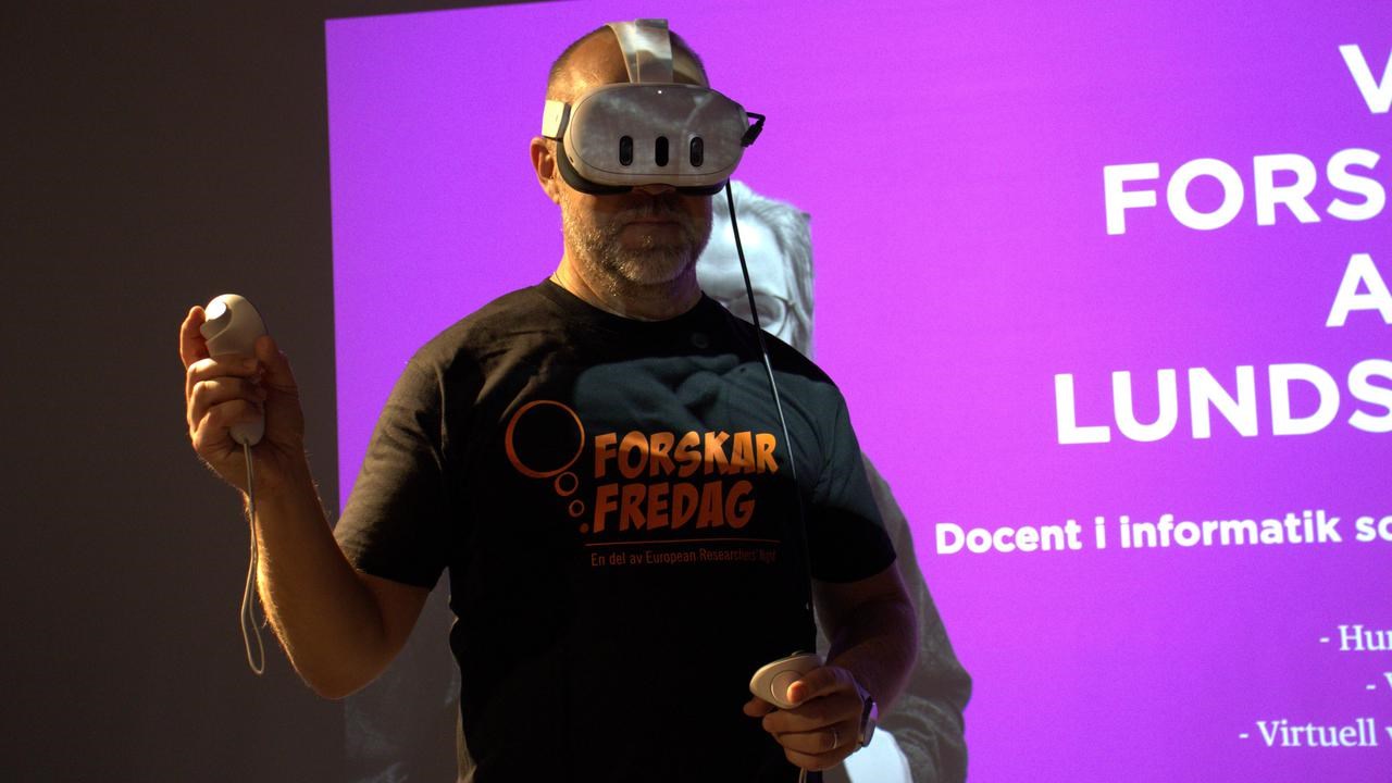 En man med ett virtuellt headset står framför en skärm.