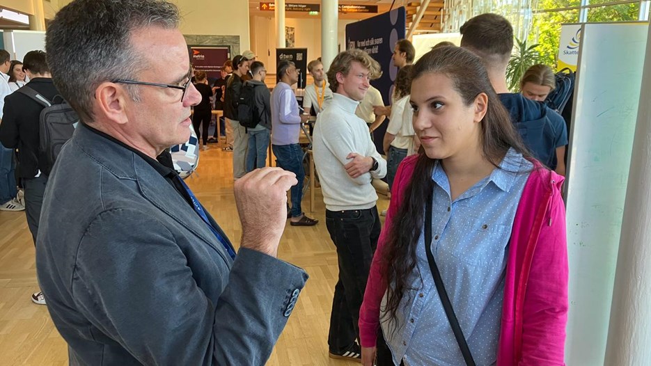 Bild på Anders Sjövik och Simona Ebid i samtal under mingel bland företagsmontrar.