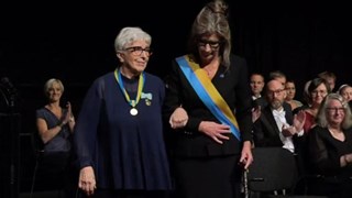 Två kvinnor i armkrok går fram på en scen.