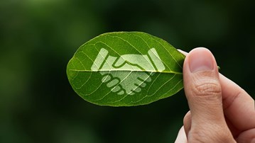 Fingrar som håller i ett löv. På lövet finns en symbol på två händer som skakar hand.