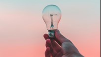 En hand som håller upp en glödlampa mot en rosa och blå bakgrund