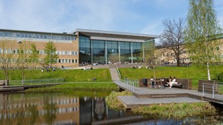 Lindellhallen och Samhällsvetarhuset sedda från campusdammen på våren.