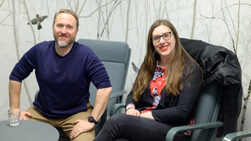 Eric Libby and Laura Carroll sit in IceLab against a background wallpaper of birds