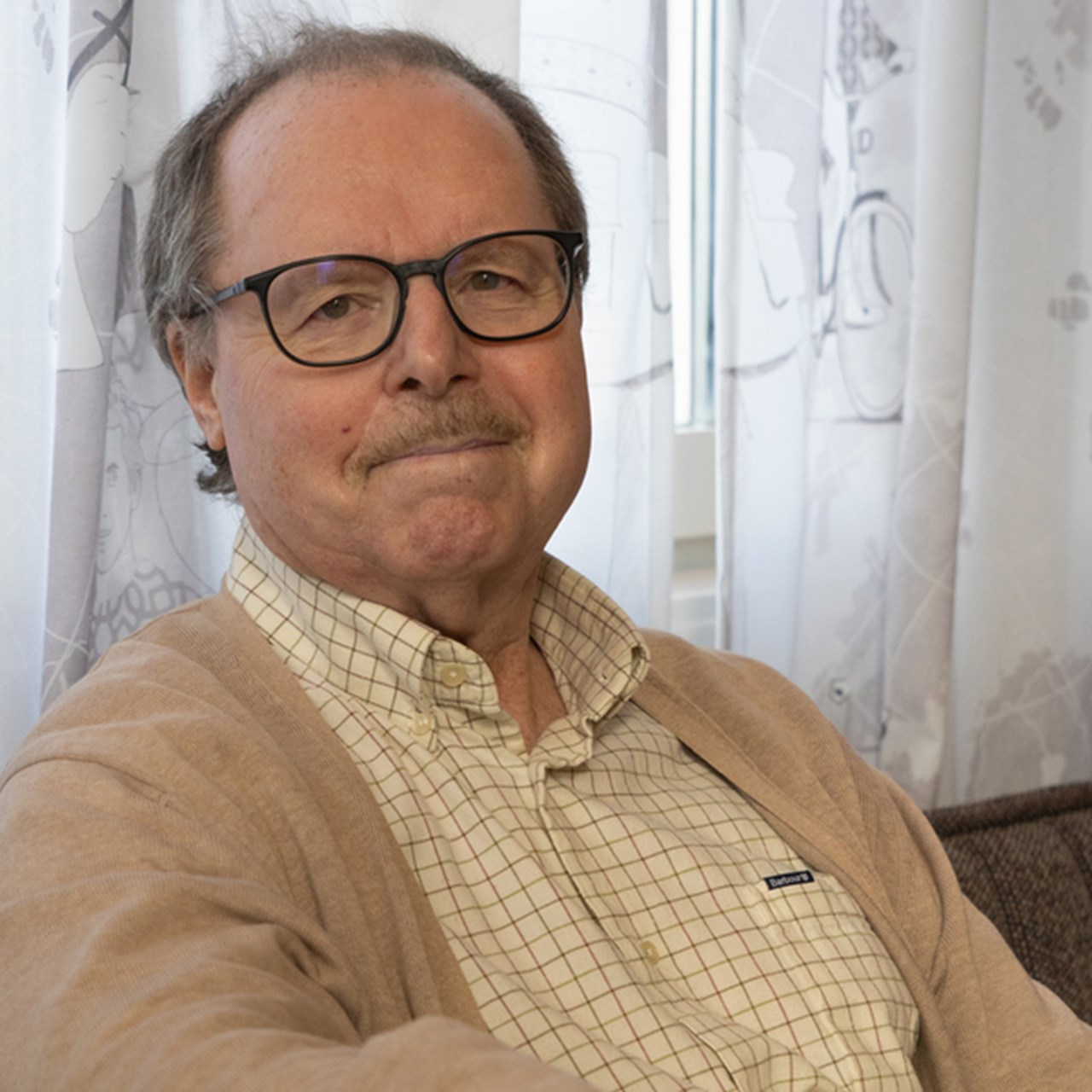 En man med glasögon sitter i en soffa.