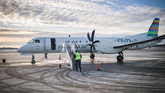 Ett flygplan som står på landningsplattan på Umeå flygplats. En flygplatsanställd håller på att ansluta trappan för att passagerare ska kunna gå ur planet.