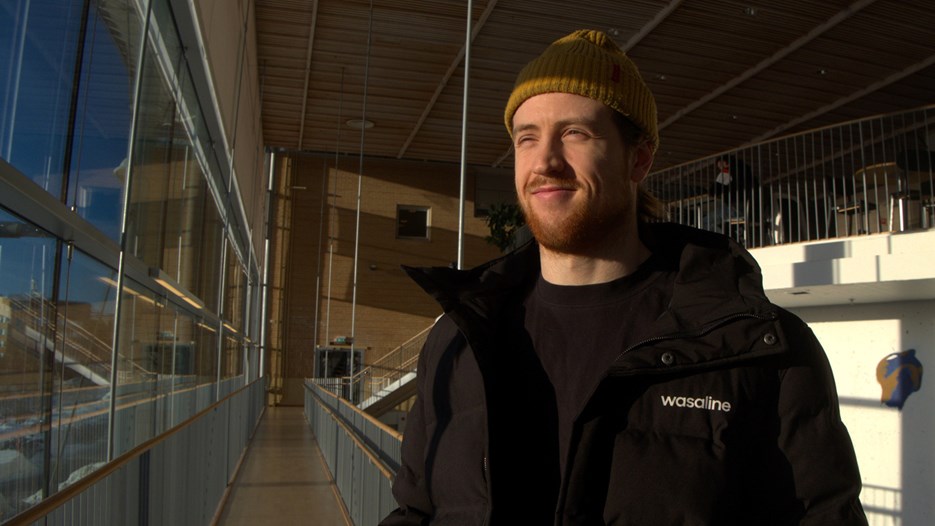 Student som tittar ut genom de stora fönstren i Lindellhallen vid Umeå universitet.