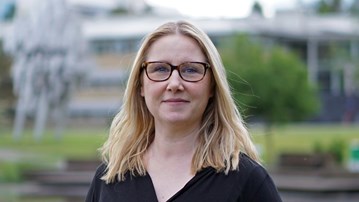 En kvinna med glasögon står framför en damm.