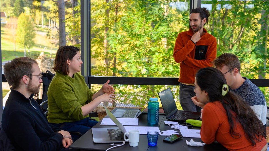 Four people seated look up towards a standing man and converse together