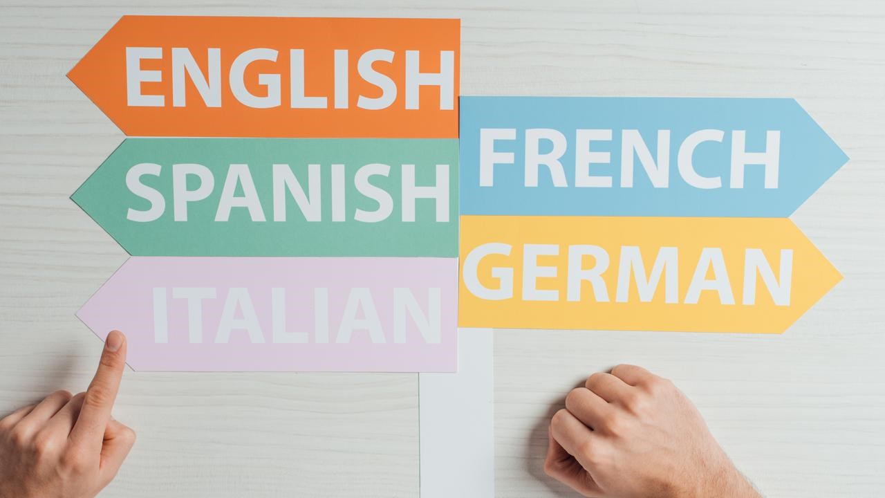 Skyltar med olika språk på som pekar åt olika håll som en hand pekar på. För att illustrera språkinlärning eller livslångt lärande.