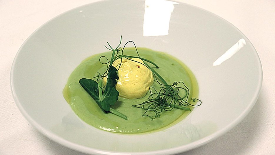 En vit tallrik med kall grön ärtsoppa, toppad med gurkmeja grädde.