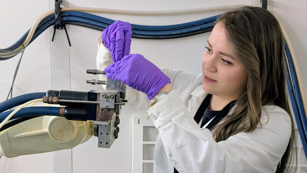 En kvinna i labbrock och handskar arbetar på en maskin.