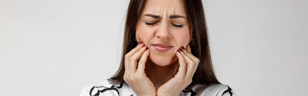 Kvinna med tandvärk som håller om käkarna och grimaserar.