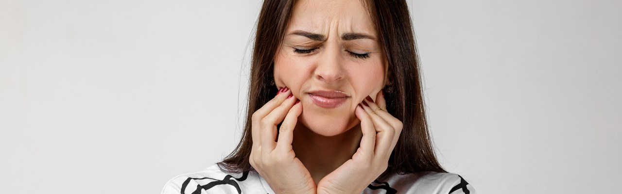 Kvinna med tandvärk som håller om käkarna och grimaserar.