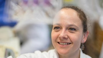 Kvinnlig forskare tittar på provrör som hon håller upp.