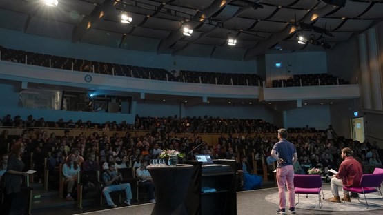 A man standing on a stage in front of a crowd of international students