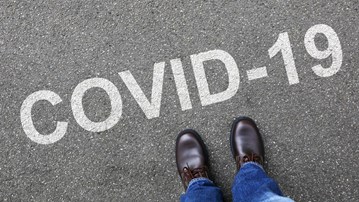 Fötter som står framför ordet Covid-19 skrivet på asfalten.