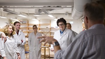 Pepole in lab coats listening to a male professor