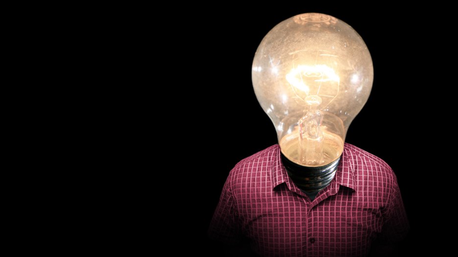 Picture of the upper half a mans body in a pink shirt, His head is a lit light bulb.